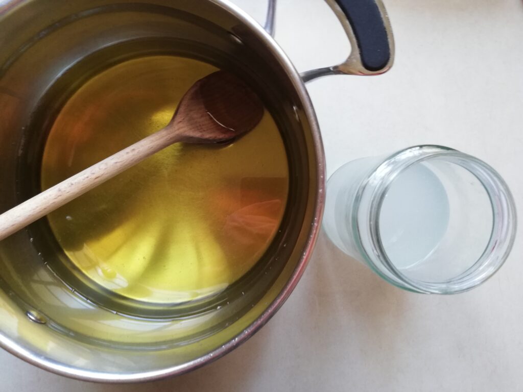 pot with melted fats and oils and a wooden spoon on the left and a jar with lye solution on the right