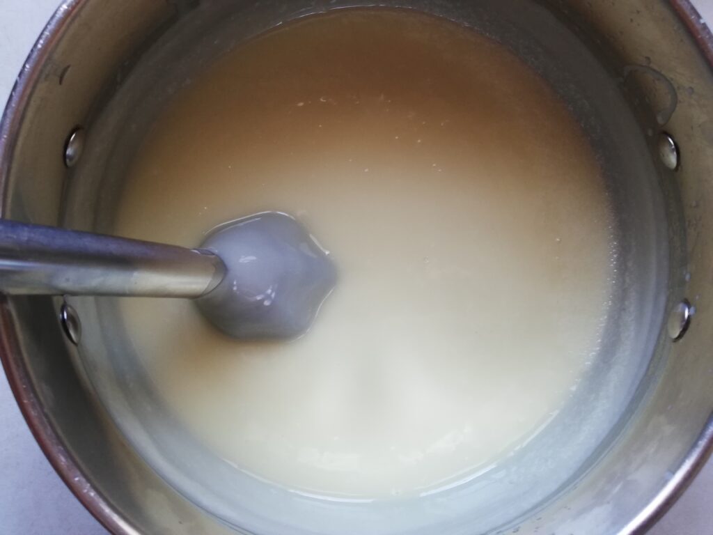 a metal pot with lye water and oils mized and emulsified and a stick blender inserted