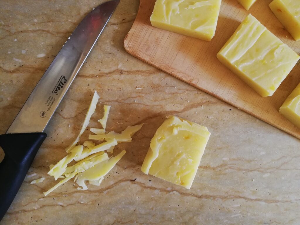 a bar of pumpkin spice soap with some soap shavings and a knife on the left and some more bars of soap on a wooden tray above