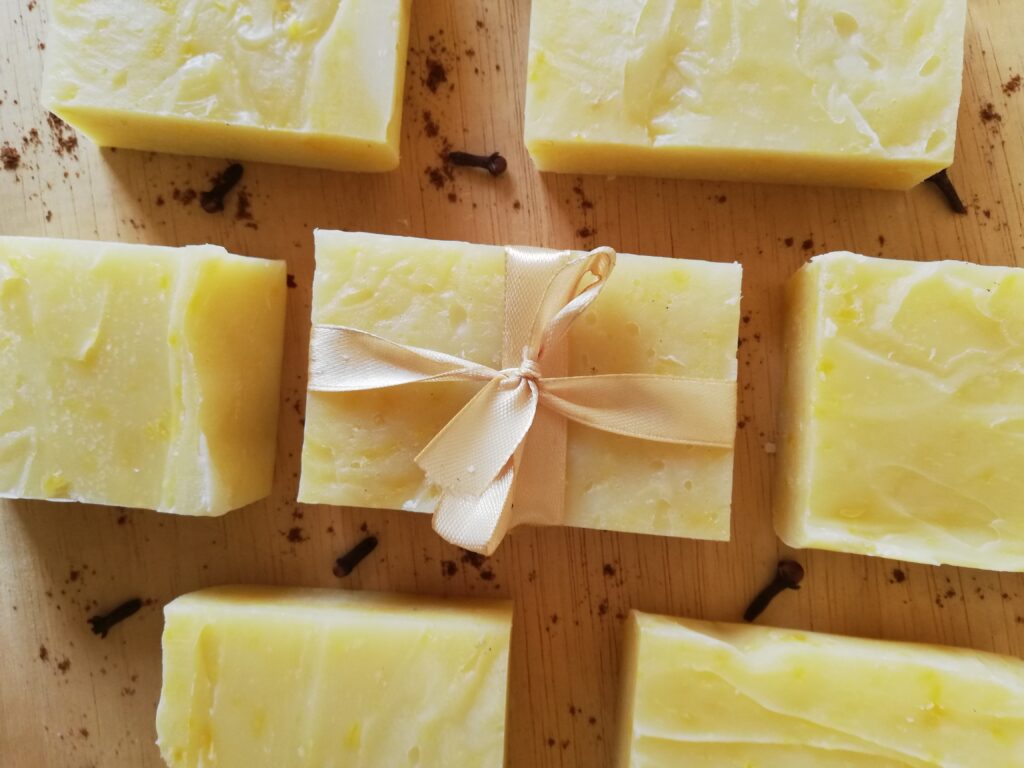 bars of pumpkin spice soap on a wooden tray with cloves and cinnamon powder sprinkled around the bar of soap in the center tied with a light golden ribbon