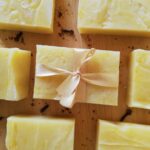 pumpkin spice soap bars on a wooden board with cloves and cinnamon powder sprinkled around with the soap in the center tied with a pink ribbon