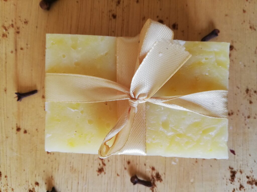 bar of pumpkin spice soap tied with a light golden ribbon on a wooden tray with cloves and cinnamon powder sprinkled around 