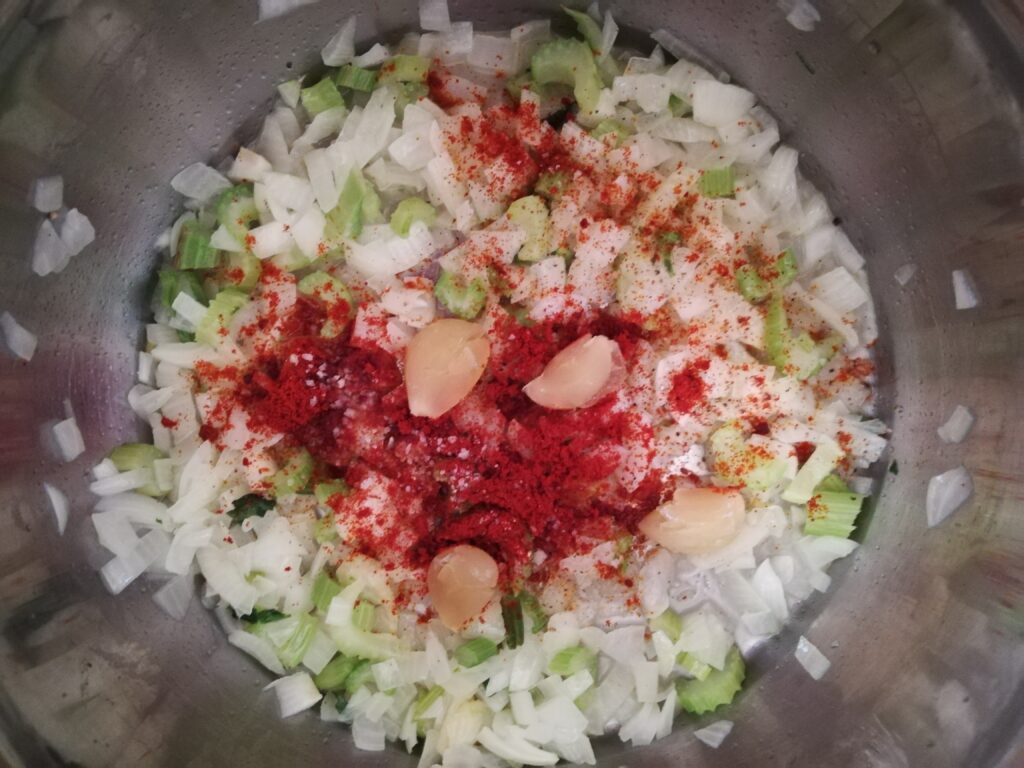chopped onions and celery peeled garlic cloves and paprika in a metal pot