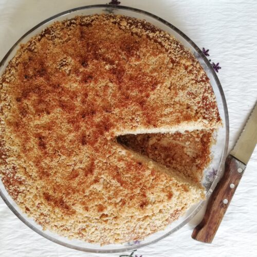 round cake dish with banana coconut discard cake with one slice cut out and a knife on the side