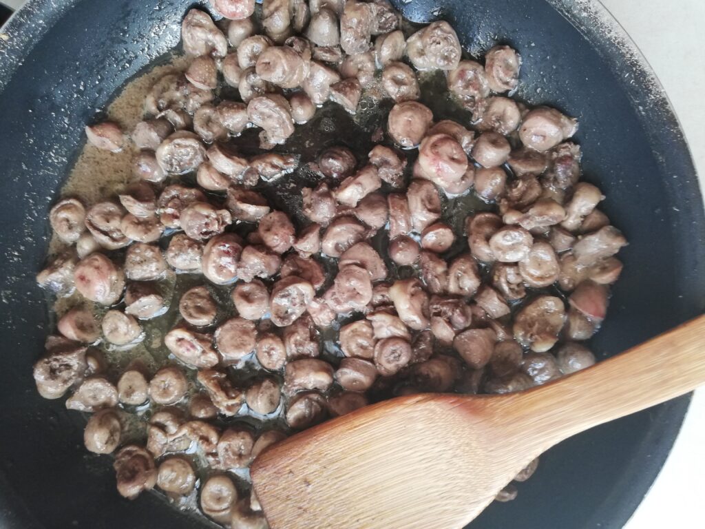 sliced chicken hearts frying in butter in a pan