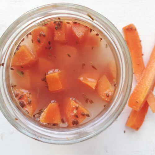 a jar of fermented carrots with dill and garlic and a few fermented carrots sticks on the side