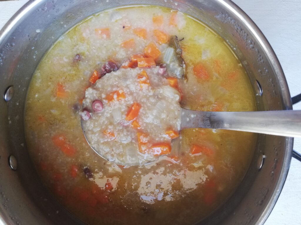 ready to eat barley soup with chicken hearts in a pot with a ladle lifting up some of the soup