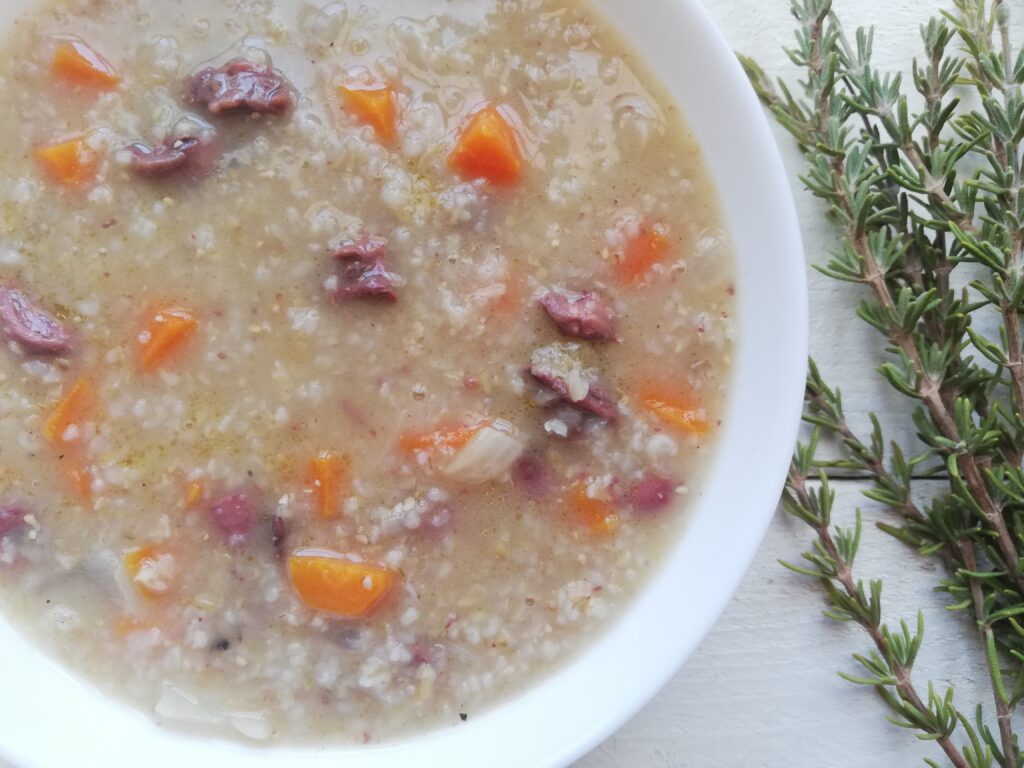 a bowl of barley soup with chicken hearts and some fresh rosemary sprigs on the side