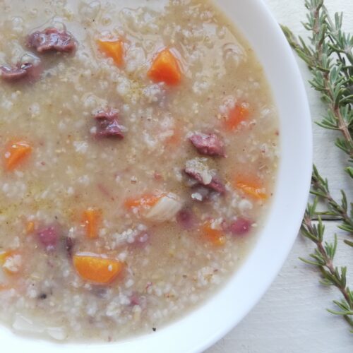 a bowl of barley soup with chicken hearts and vegetables and some fresh rosemary sprigs on the side
