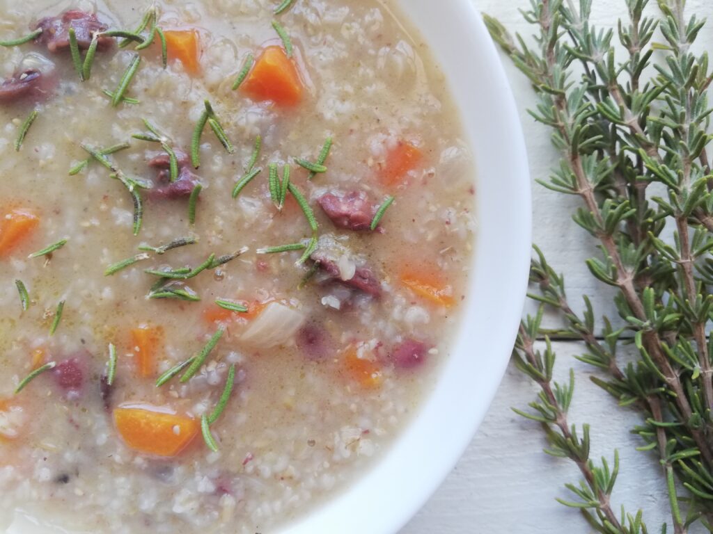 barley soup with chicken hearts in a bowl garnished with fresh rosemary with some rosemary sprigs on the side 