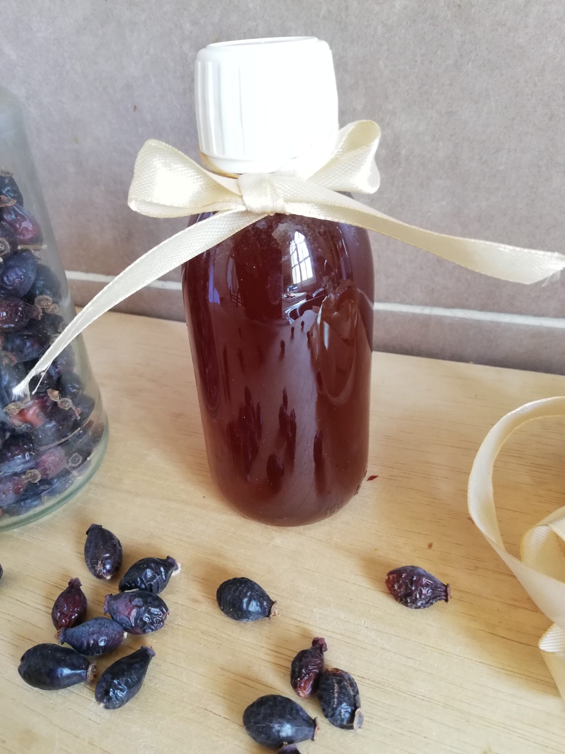 A bottle of rosehip syrup tied with a ribbon and some dried rosehips scattered around