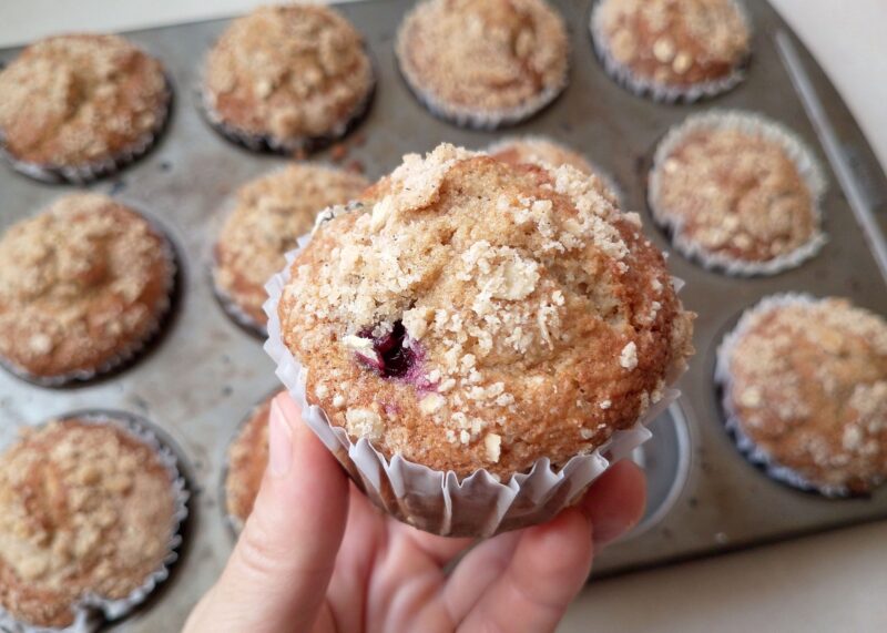 Hand holding sourdough applesauce muffin with a pan of muffins in background
