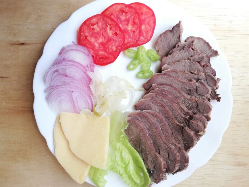 Sliced beef tongue on a platter with cheese and vegetables