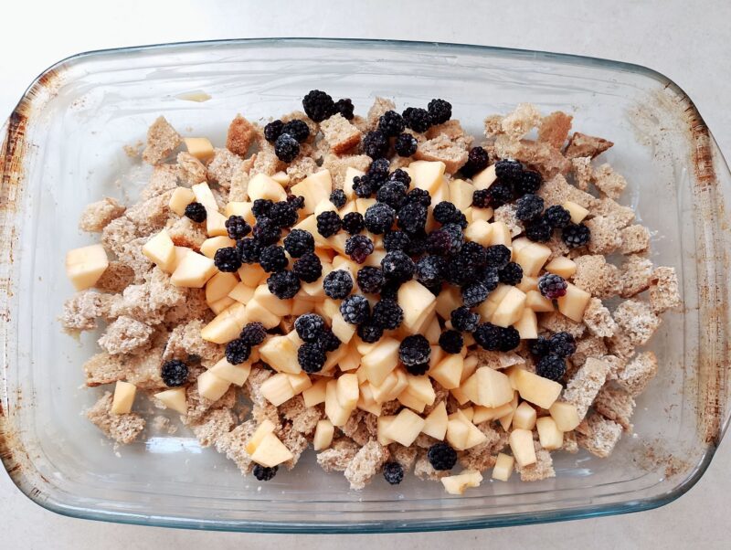 Mixing cubed bread, chopped apples, and blackberries in baking dish
