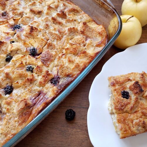 Sourdough French toast bake with apples and blackberries in a baking dish and a slice on plate