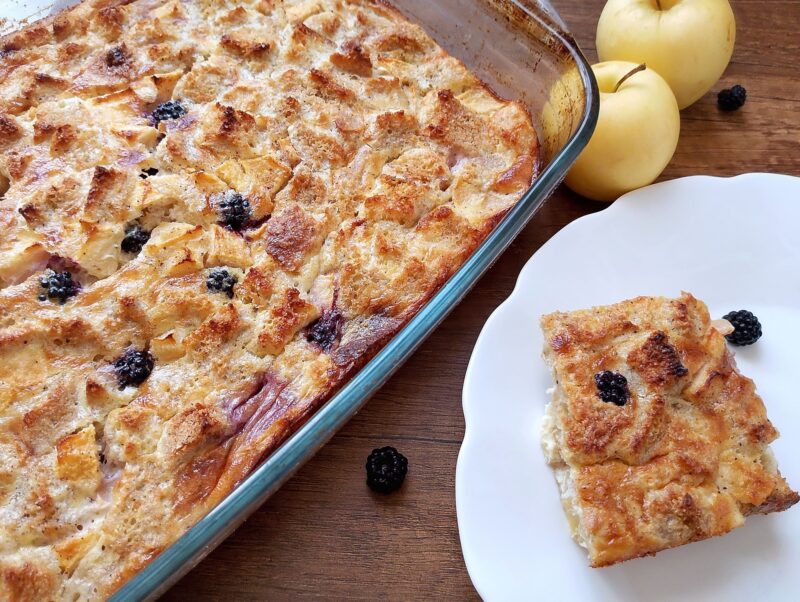Sourdough French toast bake with apples and blackberries in a baking dish and a slice on plate