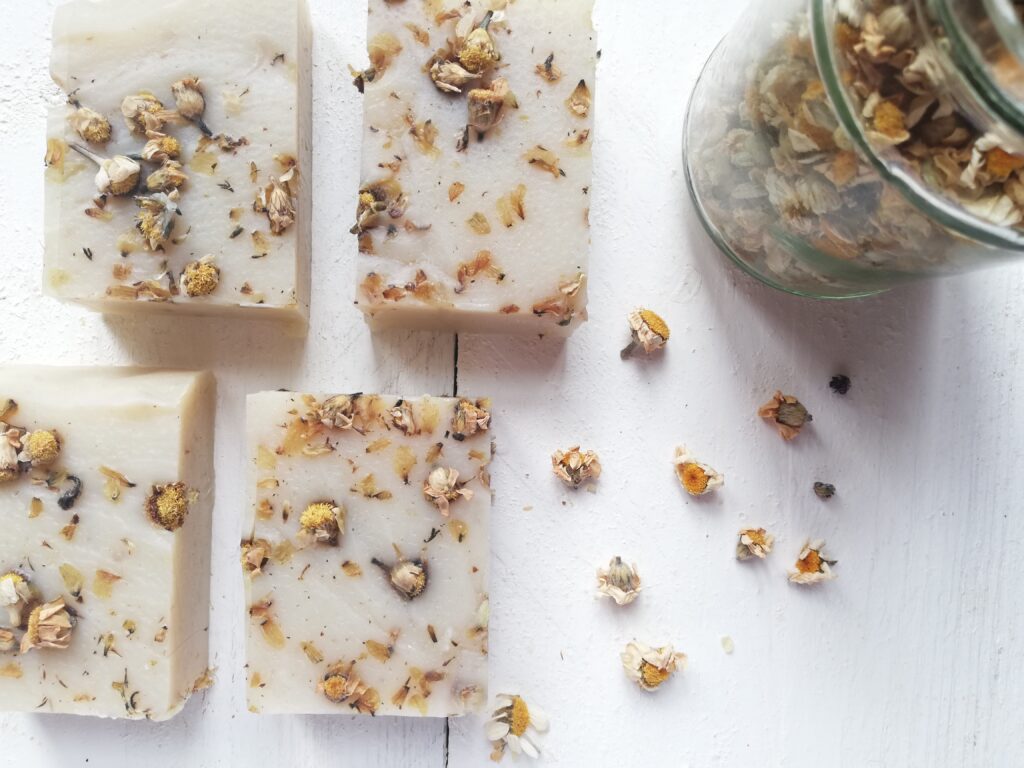 Chamomile soap on whie wooden background with a jar of chamomile flowers and some flowers sprinkled around
