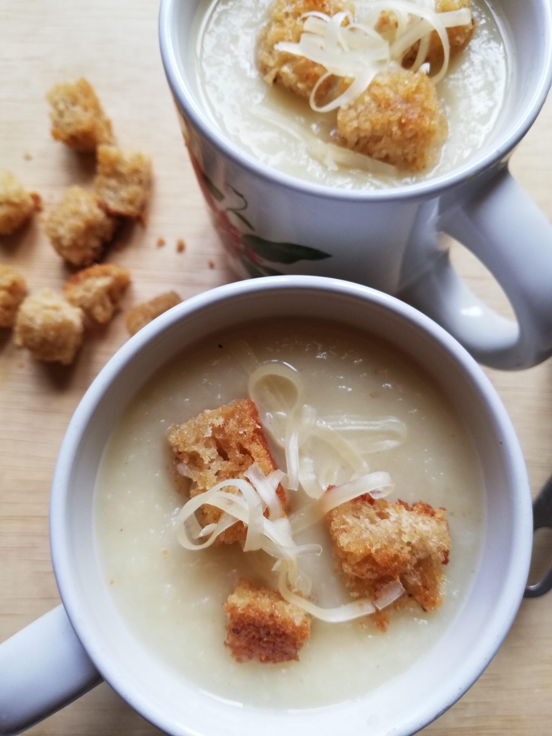 two mugs with leek and potato soup garnished with croutons and grated cheese