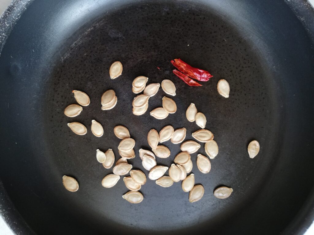 Pumpkin seeds and chilli being toasted on a dry frying pan