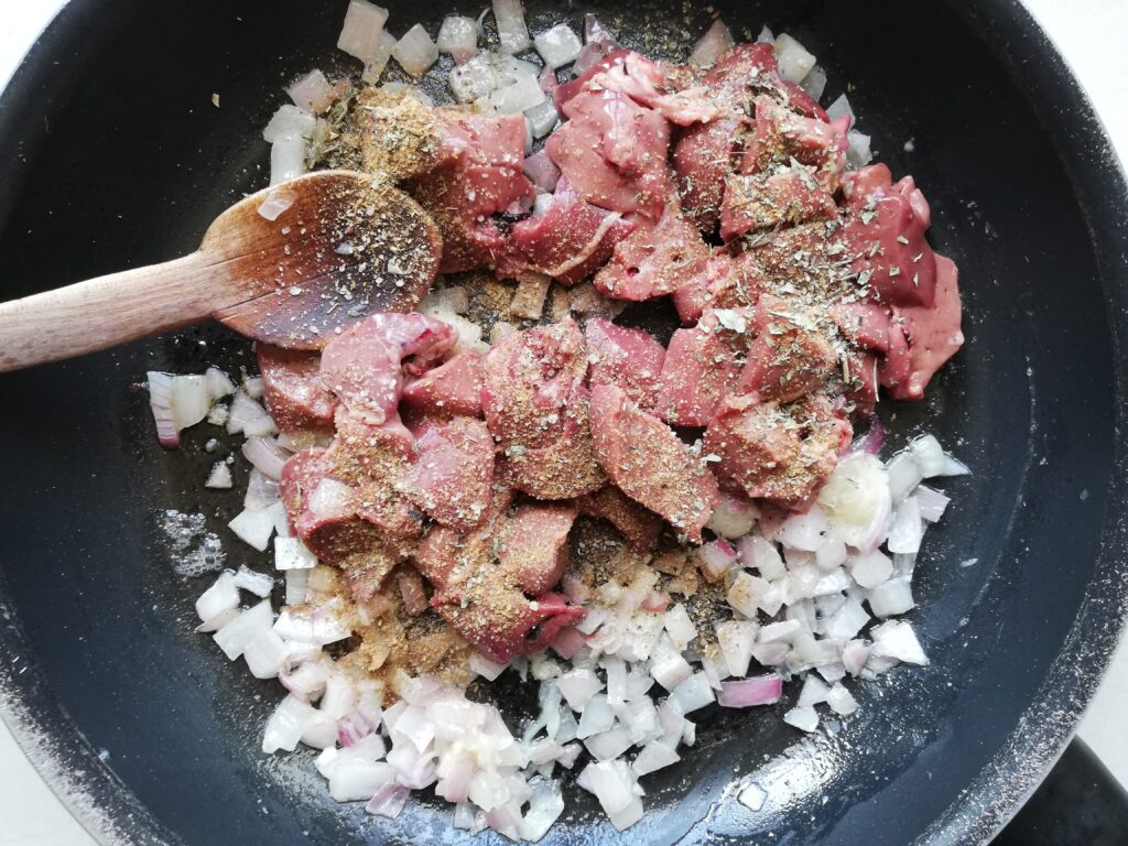 Onions, garli and raw chicken livers seasoned with oregano, cumin and coriander cooking in butter on a frying pan