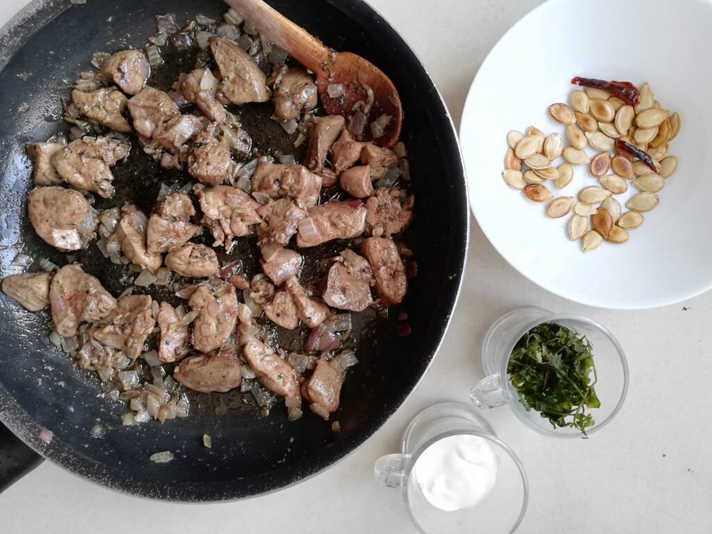 Cooked livers in a pan, a bowl of toasted pumpkin seeds and chilli, and cups with cilantro and creme fraiche