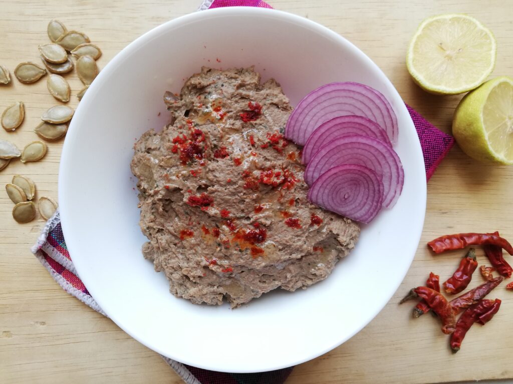 Mexican chicken liver pâté served in a white bowl with some chilli powder and a drizle of oil on top and garnished with sliced red onions