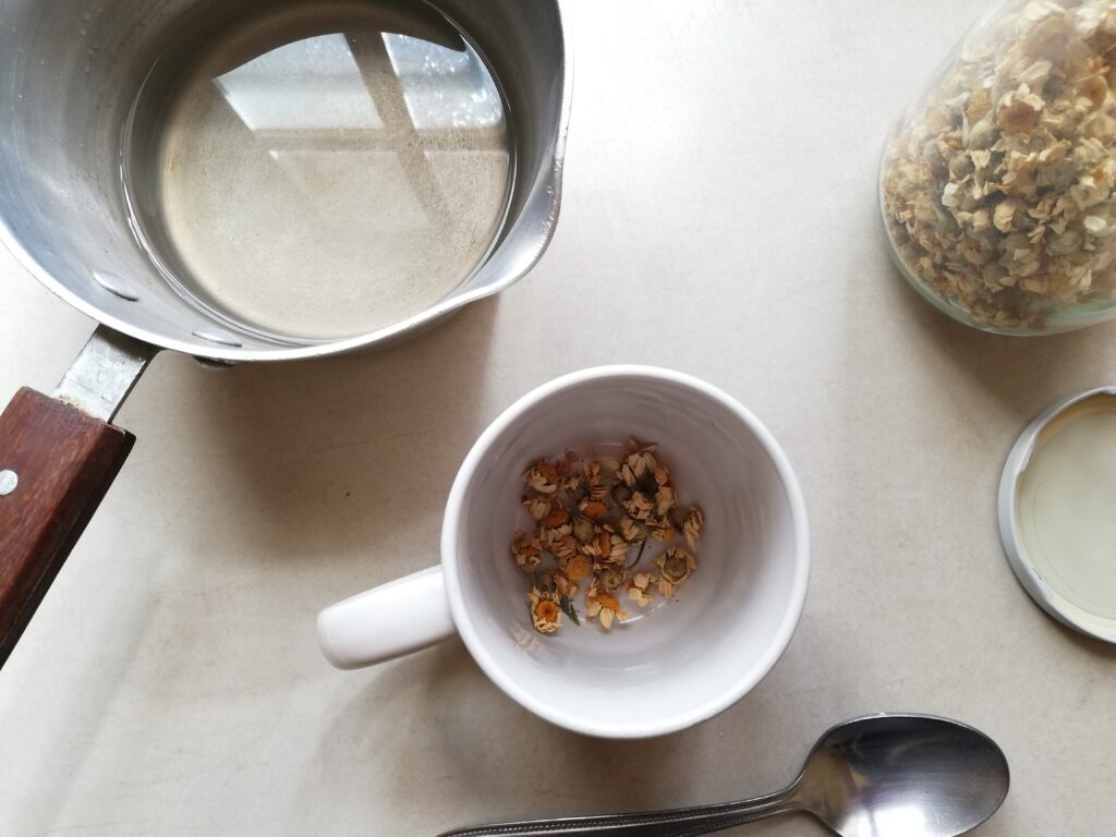 Pouring hot water over chamomile flowers in a mug to make chamomile tea for use in the soap