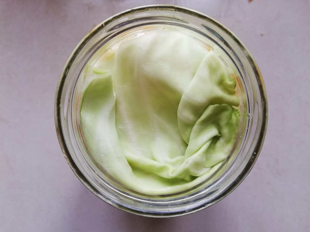 A jar full of urtido with a piece of a cabbage leaf on top