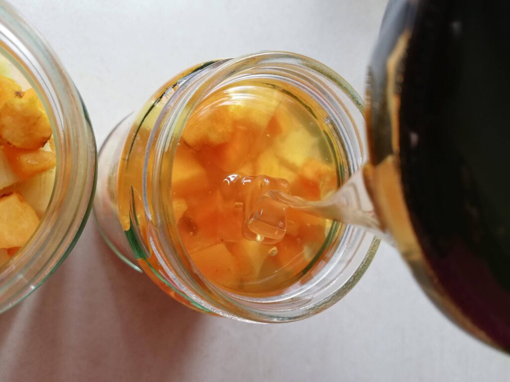 Pouring raw honey over chopped turmeric and ginger in jars