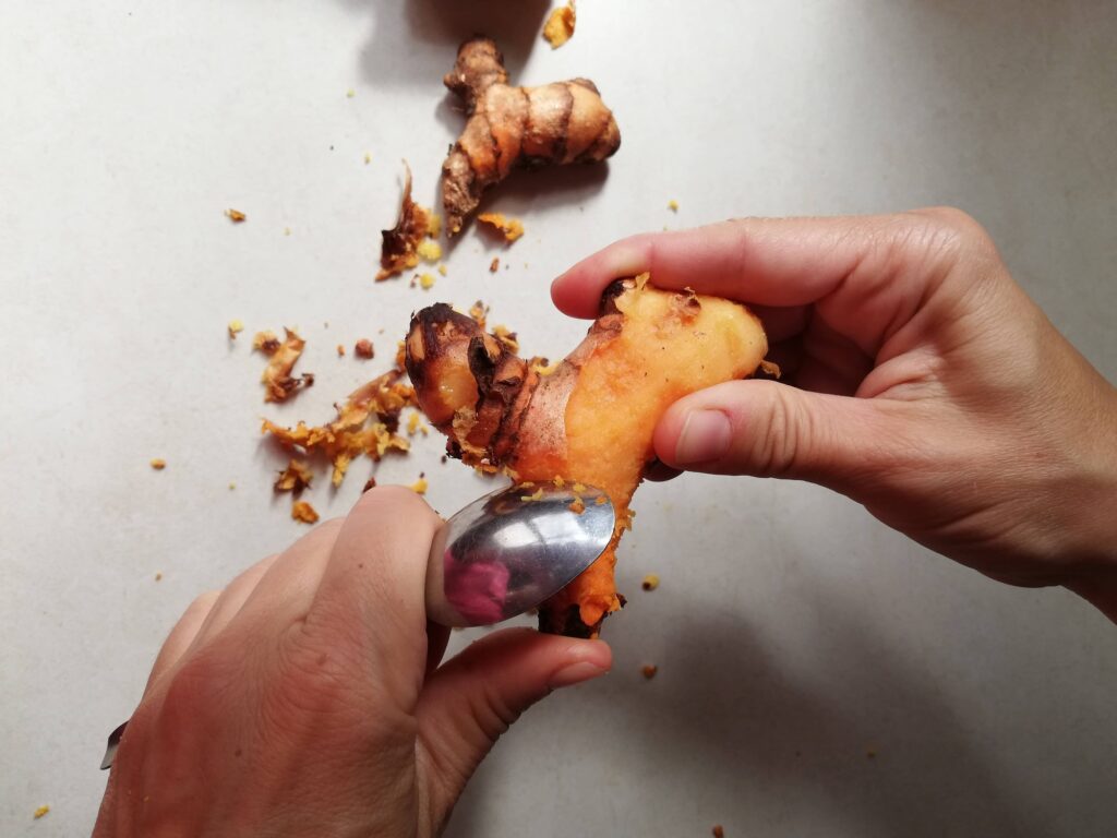 Peeling fresh turmeric root with the side of a teaspoon