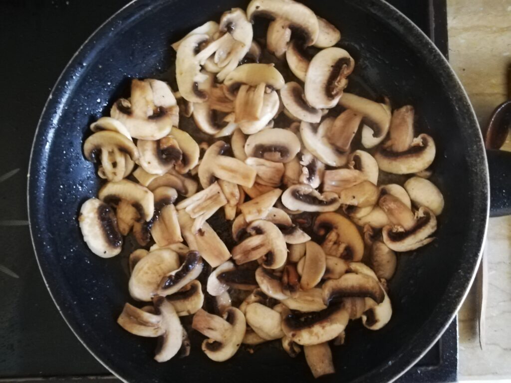 Sauteing sliced mushrooms in a frying pan