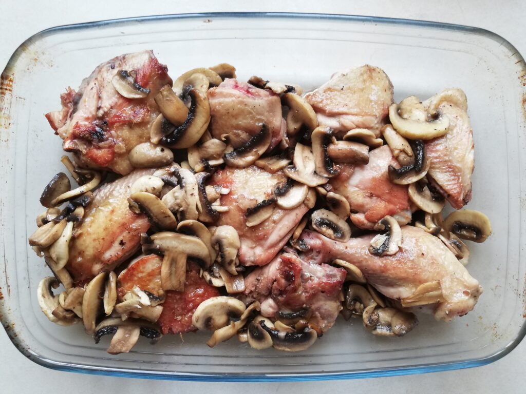 Browned chicken pieces and sauteed mushrooms in a glass casserole
