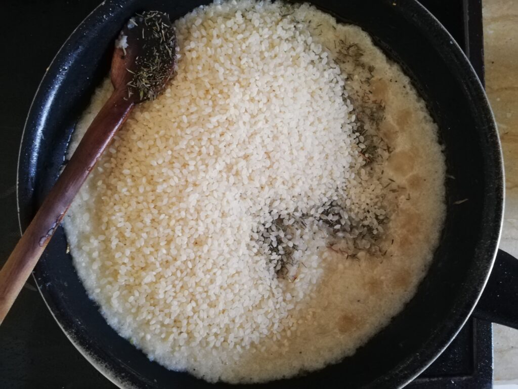 Mixing risotto rice with minced onions and garlic in a frying pan