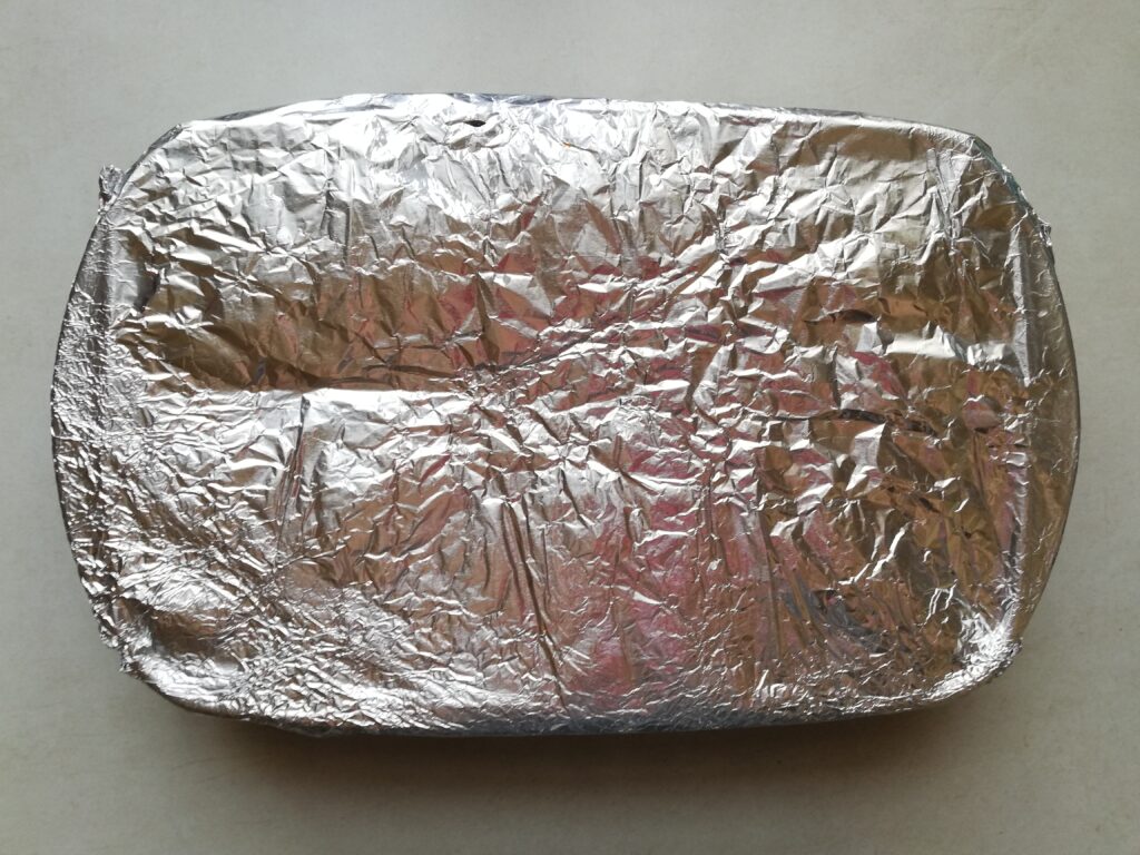 Risotto in a glass casserole covered with foil and ready to be baked