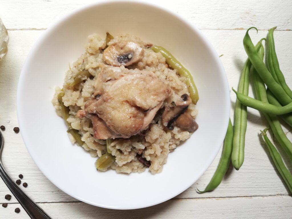 A bowl with baked risotto with a piece of chicken on top and some green beans on the side