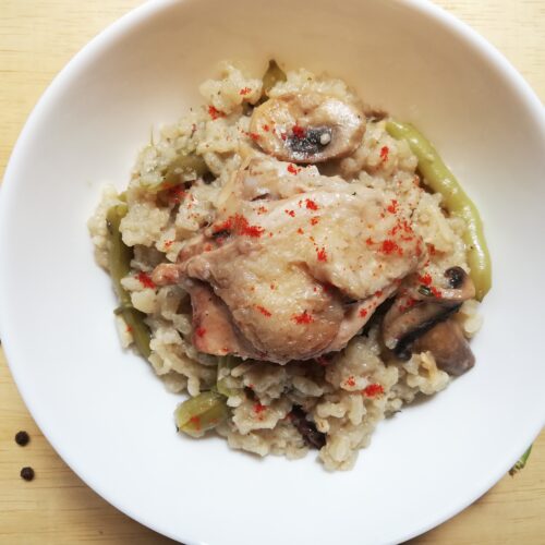 A bowl with oven risotto with chicken, mushrooms and green beans garnished with a sprinkle of paprika
