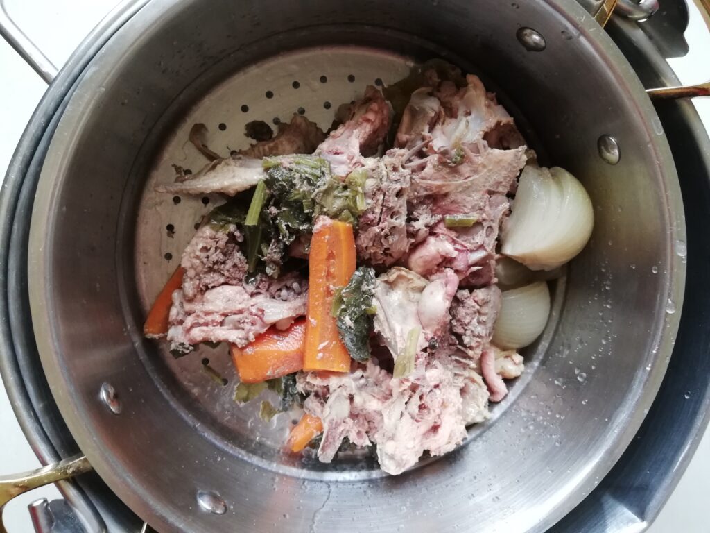 Straining chicken bone broth through a colander set over a pot