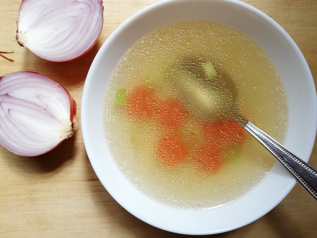 A bowl of hot chicken bone broth with some carrot and celery slices