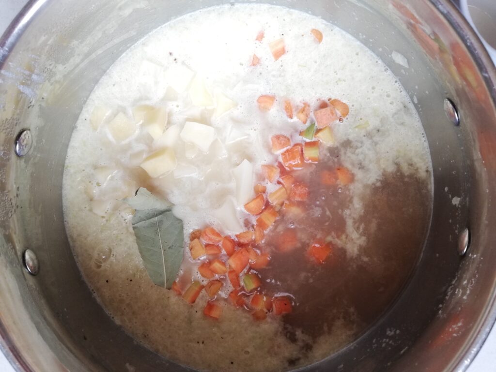 Adding the rest of the chicken stock, the carrots, the potatoes, and the bay leaf to the blended soup base
