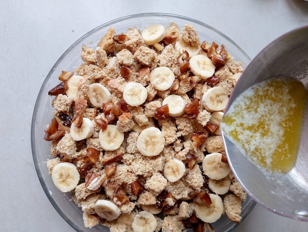 Pouring melted butter over the cubed bread, bananas and dates in the casserole dish