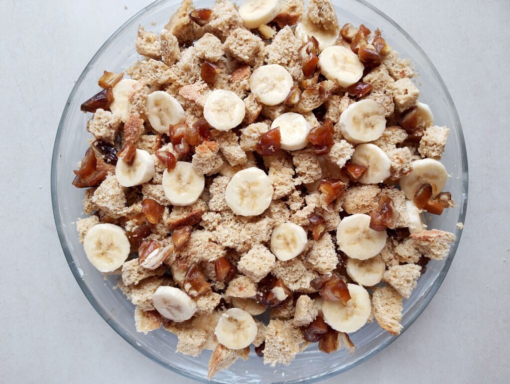 Cubed sourdough bread, sliced bananas and choppd dates arranged in layers in a round casserole dish