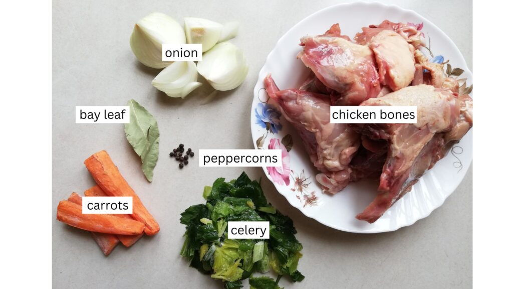 Ingredients for bone broth - chicken bones on a plate, frozen celery, carrots, bay leaf, peppercorns, and onion on a marble countertop