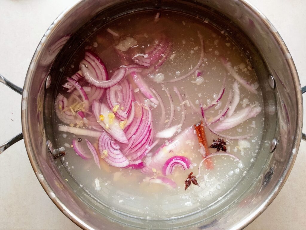 Making broth base for the Chinese noodle soup with onions, garlic, spices, and chicken bone broth