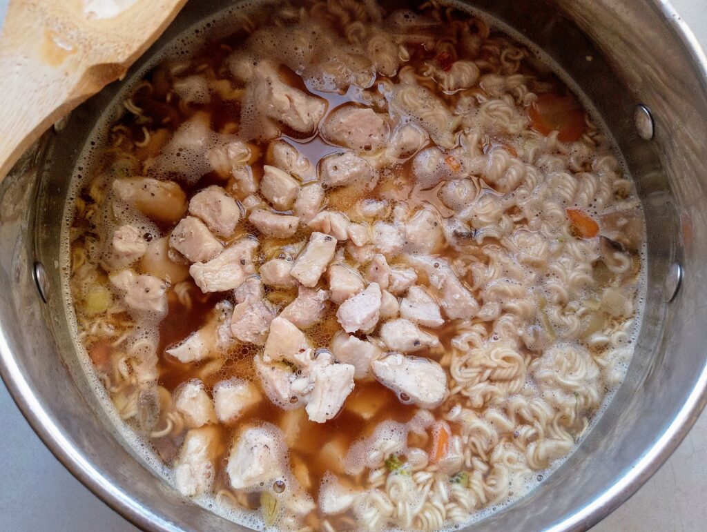 Adding cooked cubed chicken breast to the Chinese noodle soup