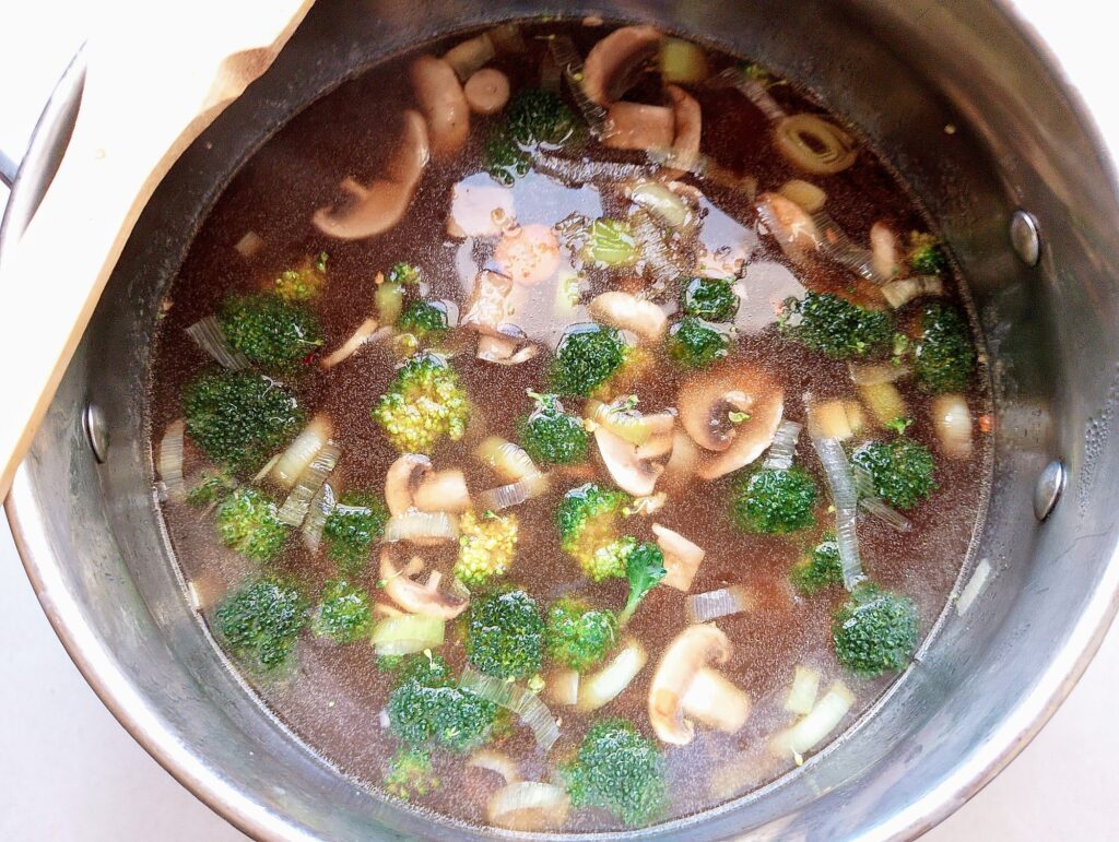 Adding prepared vegetables, soy saucem and chili flakes to the Chinese noodle soup base