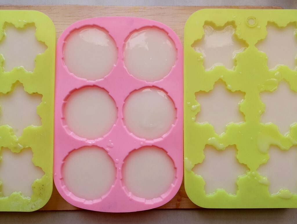Cold process coconut oil soap in molds lined up on a wooden tray