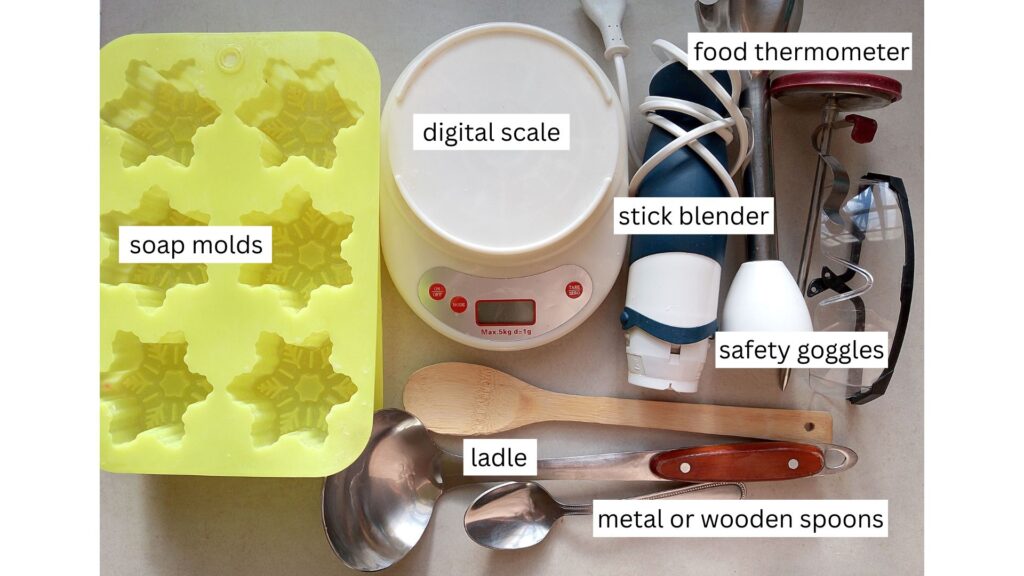 Soapmaking equipment on a counter top: soap molds, scale, stick blender, food thermometer, safety goggles. spoons, and a ladle
