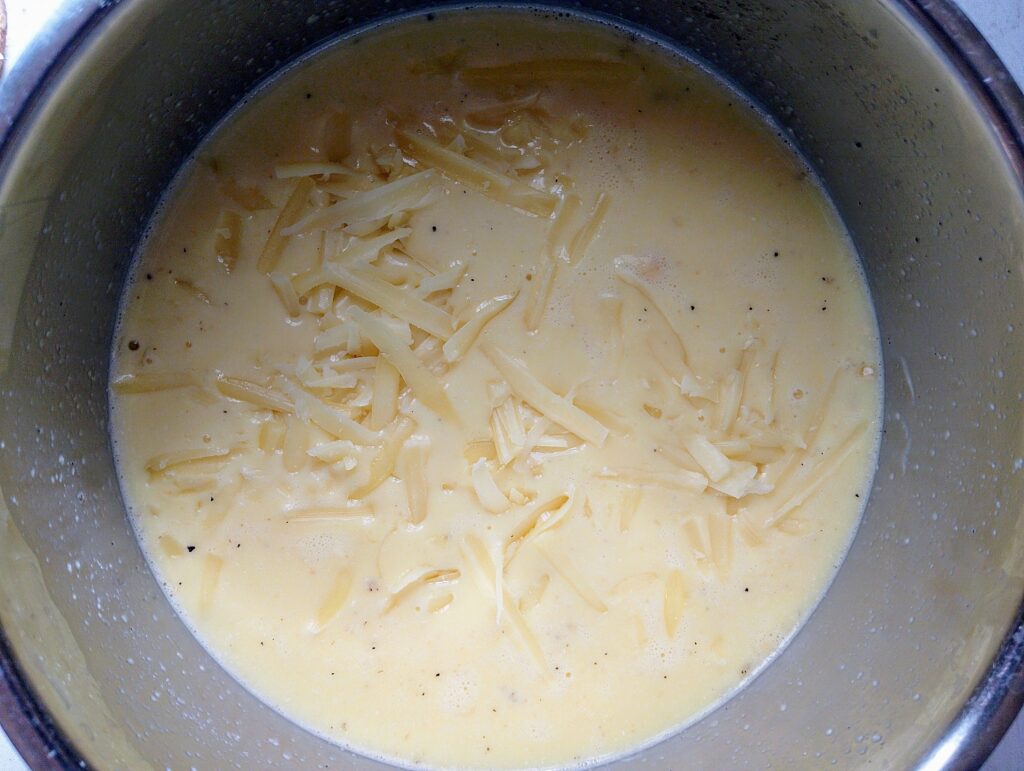 Adding shredded Cheddar cheese to the egg and milk mixture