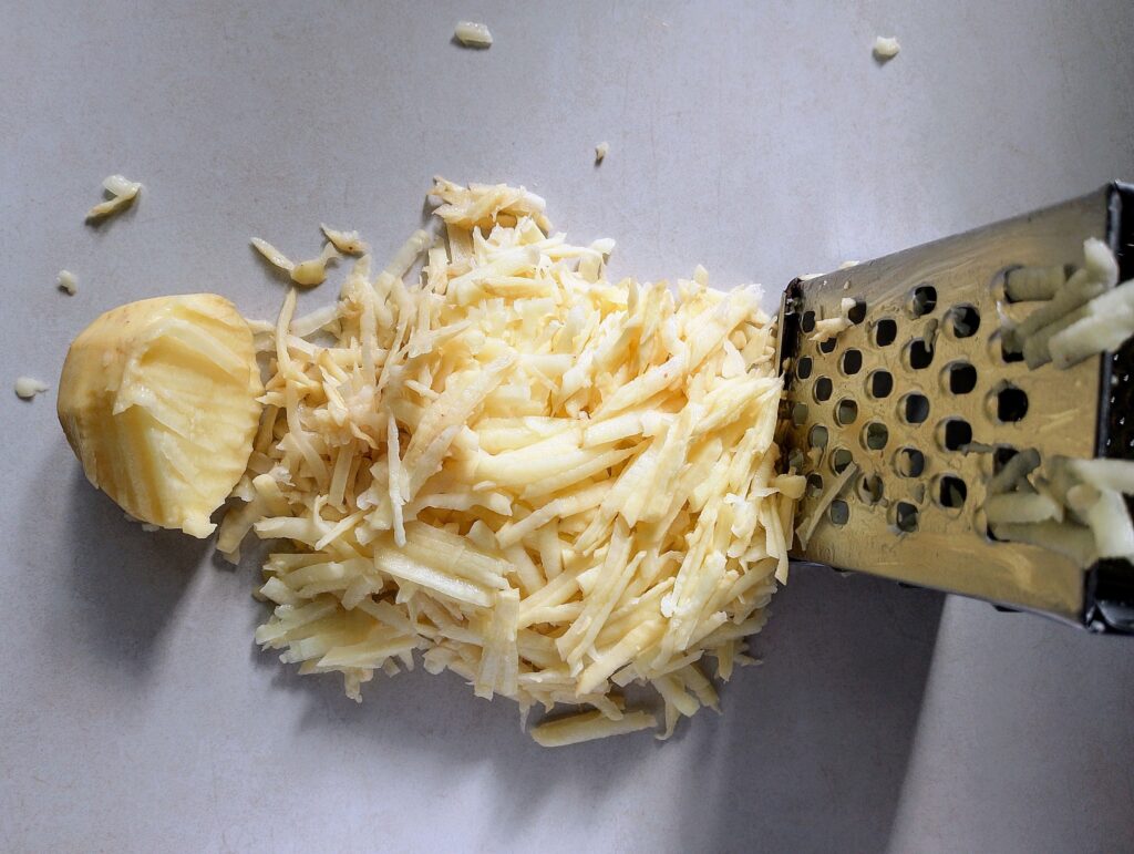 Shredding potatoes on a grater for the Amish breakfast casserole filling