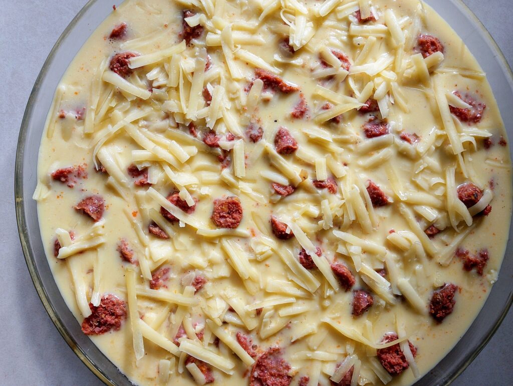 Pouring the egg, milk, and cheese filling onto the sausage, hash browns, and pepper in the baking dish